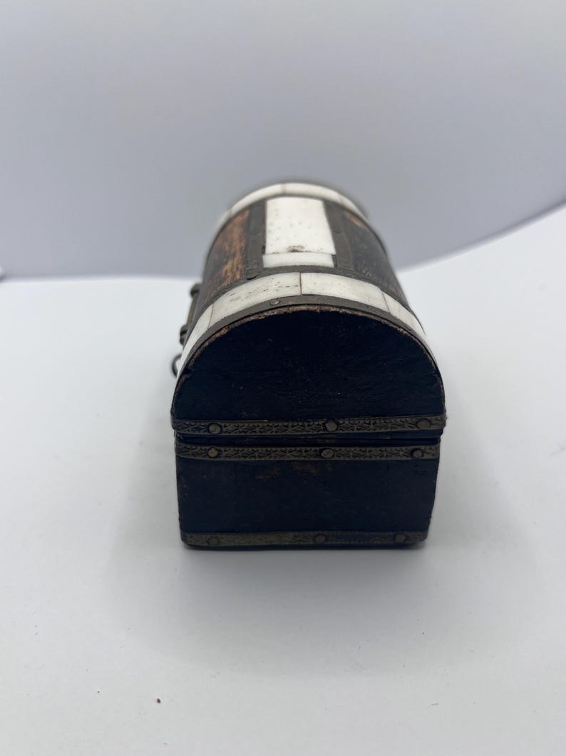 May include: A small, antique wooden chest with a rounded top. The chest is dark brown with white and silver accents. The lid and base are rectangular, and the sides are curved. The chest is likely used for storing small items.