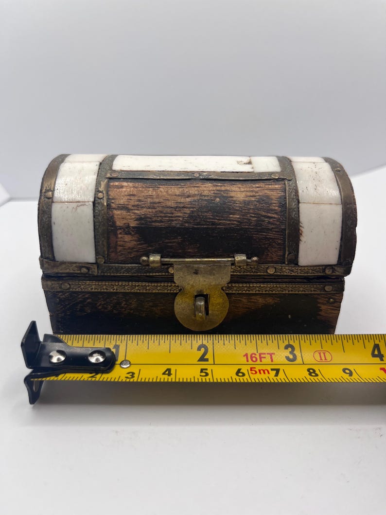May include: A small, rectangular wooden chest with a hinged lid. The chest is dark brown with white accents and metal trim. The chest is approximately 4 inches long.