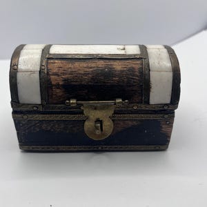 May include: A small, antique wooden chest with a hinged lid. The chest is rectangular with a curved top and is accented with white panels and metal trim. A brass clasp secures the front.