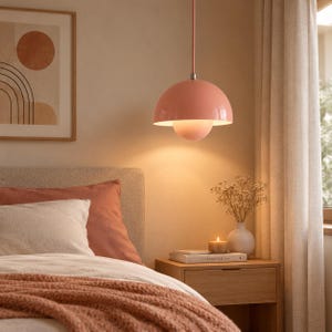 Puede incluir: Una lámpara colgante en forma de cúpula con un acabado en rosa coral suave, que presenta una pantalla interior más pequeña que difunde la luz hacia abajo. La lámpara cuelga de una varilla fina a juego sobre la mesita.