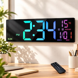 May include: A rectangular digital wall clock with a black frame and a large, multi-colored LED display showing the time 2:34 PM, the day SUN, the temperature 15°C, and the date 1/01, accompanied by a small black remote control.