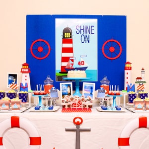 May include: A nautical themed dessert table with a blue and white tablecloth. The table is decorated with red and white striped lighthouses, blue and white striped boxes, and red and white steering wheels. The centerpiece is a white cake with a blue sailboat on top. The cake is decorated with the words "Shine On".