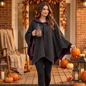 May include: A charcoal gray hooded cape with a deep purple interior lining and a single button closure at the neck. The garment features a textured fabric, a wide draped silhouette, and long sleeves, worn over solid black leggings.