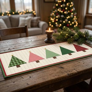 Puede incluir: Un camino de mesa rectangular con fondo color crema y un sutil patrón de cuadrícula. Cinco aplicaciones de árboles de Navidad estilizados están dispuestas en fila, cada una con una pequeña estrella dorada y un tronco marrón.