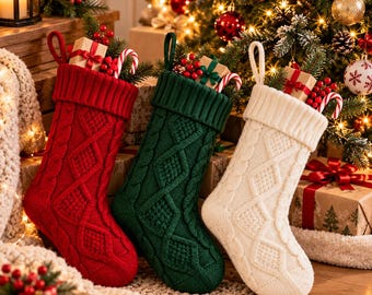 以下が含まれることがあります： 赤、ダークグリーン、クリーム色のケーブルニット製クリスマスストッキング3足。各ストッキングにはリブ編みのカフとダイヤモンド模様が施されています。小さなギフトボックス、赤いベリー、キャンディケインが詰められており、吊り下げ用のループが付いています。
