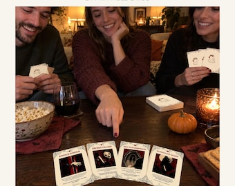 May include: A Halloween party game set featuring 24 printable cards with dark, thematic illustrations and text. The cards include titles such as Knock Knock, Secret Villain, Pick Your Nightmare, and Famous Last Words, displayed on a wooden table.