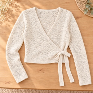 Puede incluir: Una blusa cruzada de manga larga en color crema con un patrón de punto abierto y texturizado. La prenda tiene un escote en V y un cierre lateral con dos cintas de tela a juego que sujetan los paneles delanteros en la cintura.