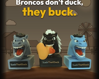 May include: Three horse head figurines on rectangular bases with the text %uckThatDuck. The left is gray, the center is black with a white mane holding an orange rubber duck, and the right is light blue. Text above reads: Broncos don't duck, they buck.