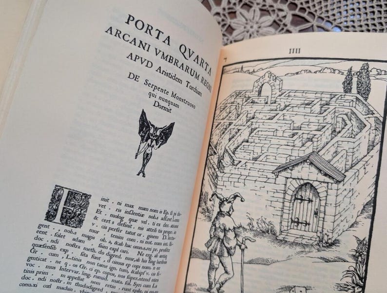 May include: Open book with text and illustrations. The left page features text in Latin and a small illustration of a winged figure. The right page shows a detailed drawing of a stone maze with a figure in the foreground.