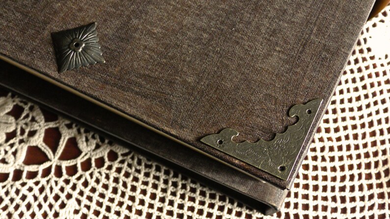 May include: A brown leather-bound journal with metal corner accents and a decorative metal piece on the front cover. The journal is resting on a white crocheted doily.