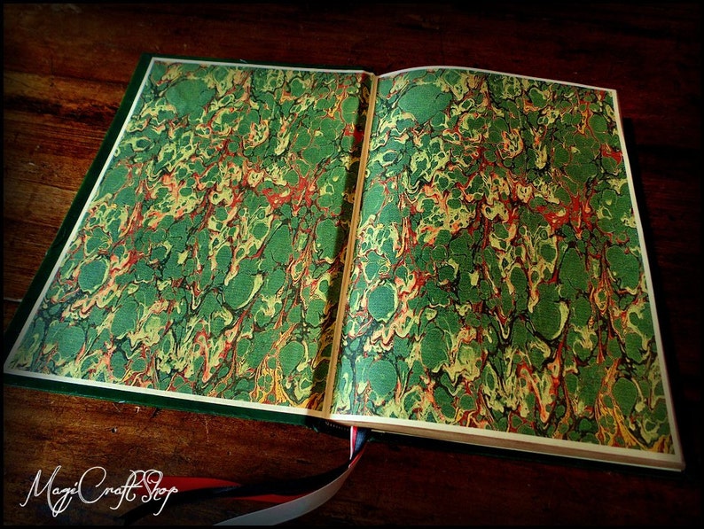 Puede incluir: Un libro abierto con una cubierta de m&aacute;rmol verde, amarillo y rojo. El libro est&aacute; abierto sobre una superficie de madera.