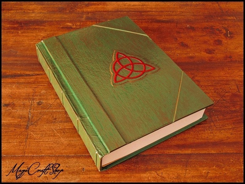 Puede incluir: Un diario encuadernado en cuero verde con un dise&ntilde;o de nudo celta rojo y dorado en la portada.