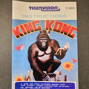 May include: A Tigervision King Kong video game instruction manual for the Atari Video Computer System or Sears Tele-Games. The cover features a large gorilla holding a figure, red airplanes, and yellow explosions on a blue background.
