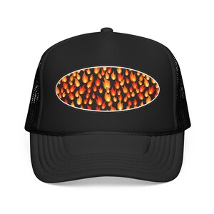 Può includere: Un cappellino trucker nero con una toppa ovale centrale sul pannello frontale. La toppa mostra un motivo ripetuto di fiamme arancioni, gialle e rosse su sfondo nero. Il cappellino ha una parte anteriore solida e una parte posteriore in rete.
