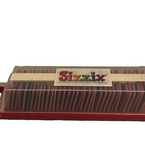 May include: A red Sizzix die-cutting machine storage case with a clear lid. The case has a handle and contains numerous red and black die-cut shapes. The Sizzix logo is visible on the front.