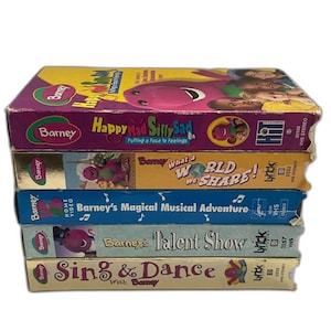May include: A stack of five Barney VHS tapes. The tapes have titles such as "Happy Mad Silly Sad", "What a World We Share!", and "Barney's Magical Musical Adventure". The tapes are in various colors, including purple, yellow, and blue.