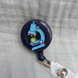 May include: A blue retractable badge holder with a microscope and green bacteria design. The badge holder has a clear plastic strap.