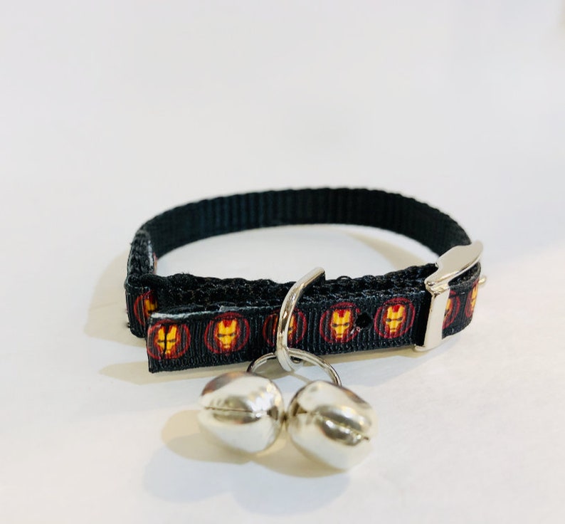 Pu&ograve; includere: Collare per gatto nero con un motivo Iron Man rosso e oro e due campanelle d'argento.