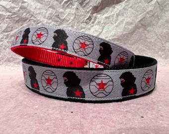 May include: A gray and black dog collar with a red and white star pattern and a silhouette of a person wearing a mask. The collar is made of a durable, high-quality material.