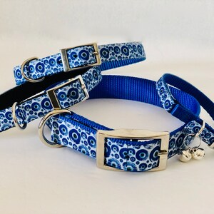 May include: A selection of blue and white patterned pet collars with silver metal buckles and D-rings. The collars display a repeating pattern of blue circles on a white background. One collar has a black interior and small silver bells.