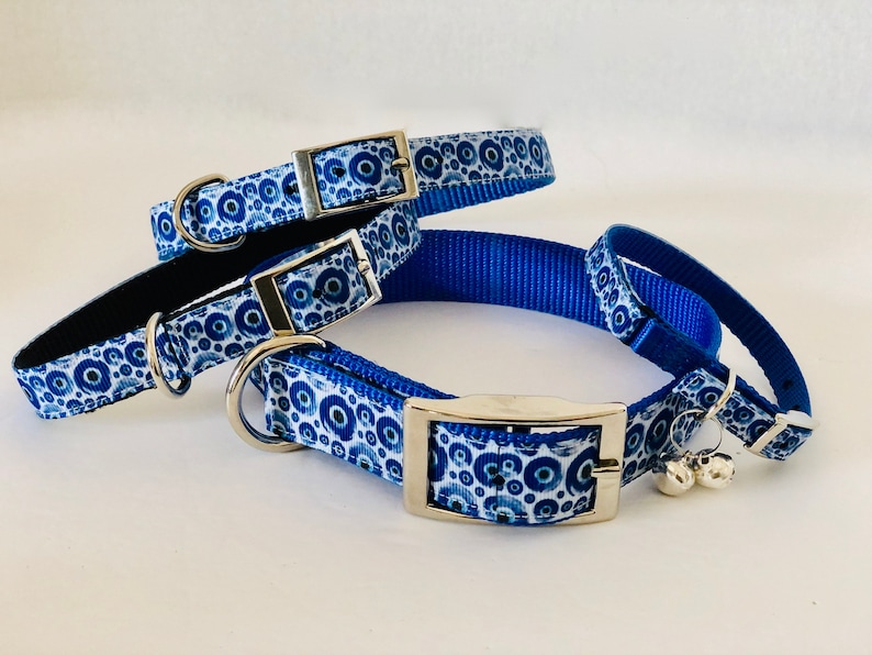 May include: A selection of blue and white patterned pet collars with silver metal buckles and D-rings. The collars display a repeating pattern of blue circles on a white background. One collar has a black interior and small silver bells.