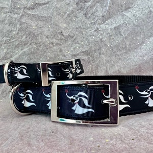 Puede incluir: Dos collares de perro negros con hebillas plateadas. Los collares presentan un patrón repetido blanco y rojo de un fantasma de la película "Pesadilla antes de Navidad".