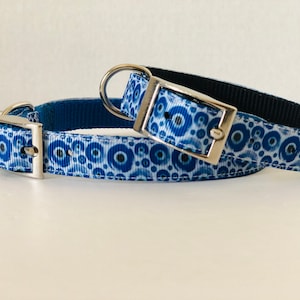 May include: Two blue dog collars with silver metal buckles. The collars have a repeating pattern of blue and white circles. One collar is on top of the other.