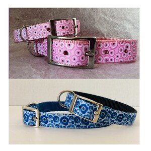May include: Two dog collars. One is pink with a white and pink circular pattern, and the other is blue with a white and blue circular pattern. Both collars have silver metal hardware.