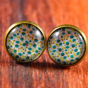 May include: A pair of round, bronze-colored earrings with a white background and a teal and yellow geometric pattern.