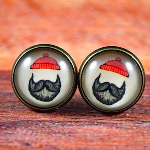 May include: A pair of round, bronze-colored earrings with a white background and a cartoon image of a black beard and red hat.