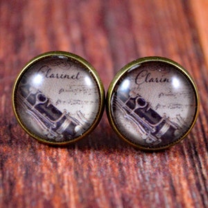 May include: A pair of gold-toned earrings with glass cabochons featuring a vintage image of a clarinet and sheet music. The text "Clarinet" is printed on the cabochons.