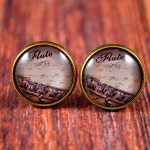 May include: A pair of gold-toned stud earrings with a glass cabochon featuring a vintage image of a flute and sheet music. The cabochons are inscribed with the word "Flute".
