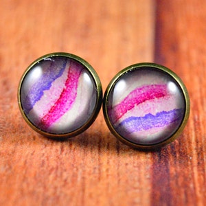 May include: A pair of stud earrings with a round, white background and a pink and purple watercolor design.