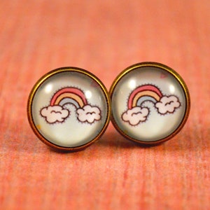 May include: A pair of gold-toned stud earrings with a rainbow and clouds design. The earrings are round and have a clear glass cabochon.