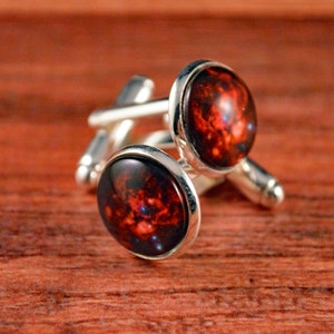 May include: A pair of silver cufflinks with a red and black galaxy design.