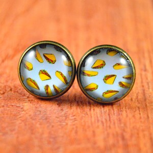 May include: A pair of round, bronze-colored earrings with a white background and a pattern of yellow tacos.