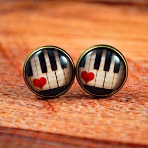 May include: A pair of round, bronze-colored earrings with a white and black piano keyboard design and a red heart on each earring.