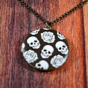 May include: A silver chain necklace with a round pendant featuring a black and white skull and rose pattern.