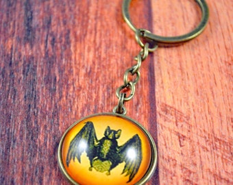 May include: A bronze key chain with a round glass charm featuring a black bat silhouette on an orange background.