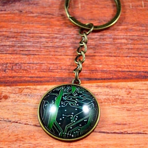 May include: A bronze key chain with a round, glass charm featuring a green circuit board design.