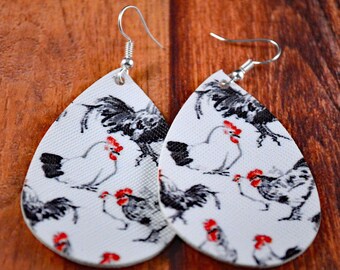 May include: A pair of white teardrop-shaped earrings with a black and white chicken print. The earrings have silver hooks.