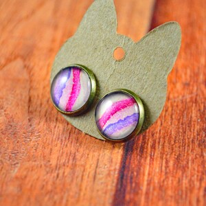 May include: A pair of earrings with a pink and purple watercolor design on a brown card.