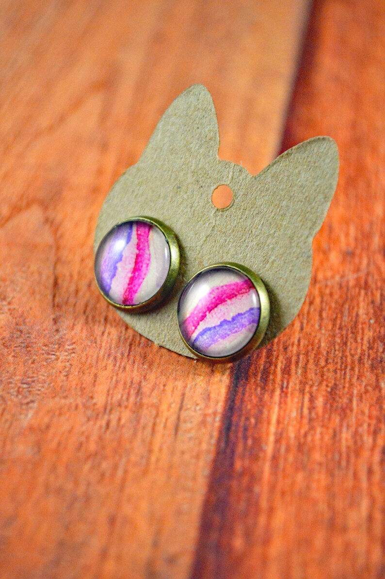 May include: A pair of earrings with a pink and purple watercolor design on a brown card.