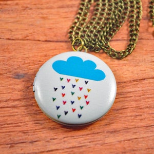 May include: A white locket necklace with a blue cloud and a rainbow of hearts falling from it. The chain is gold colored.