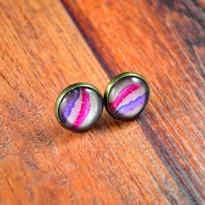 May include: A pair of stud earrings with a pink, purple, and white abstract design. The earrings have a bronze-colored setting.