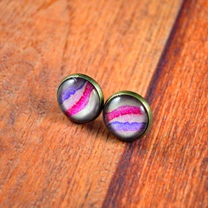 May include: A pair of stud earrings with a purple, pink, and white abstract design set in a bronze setting.