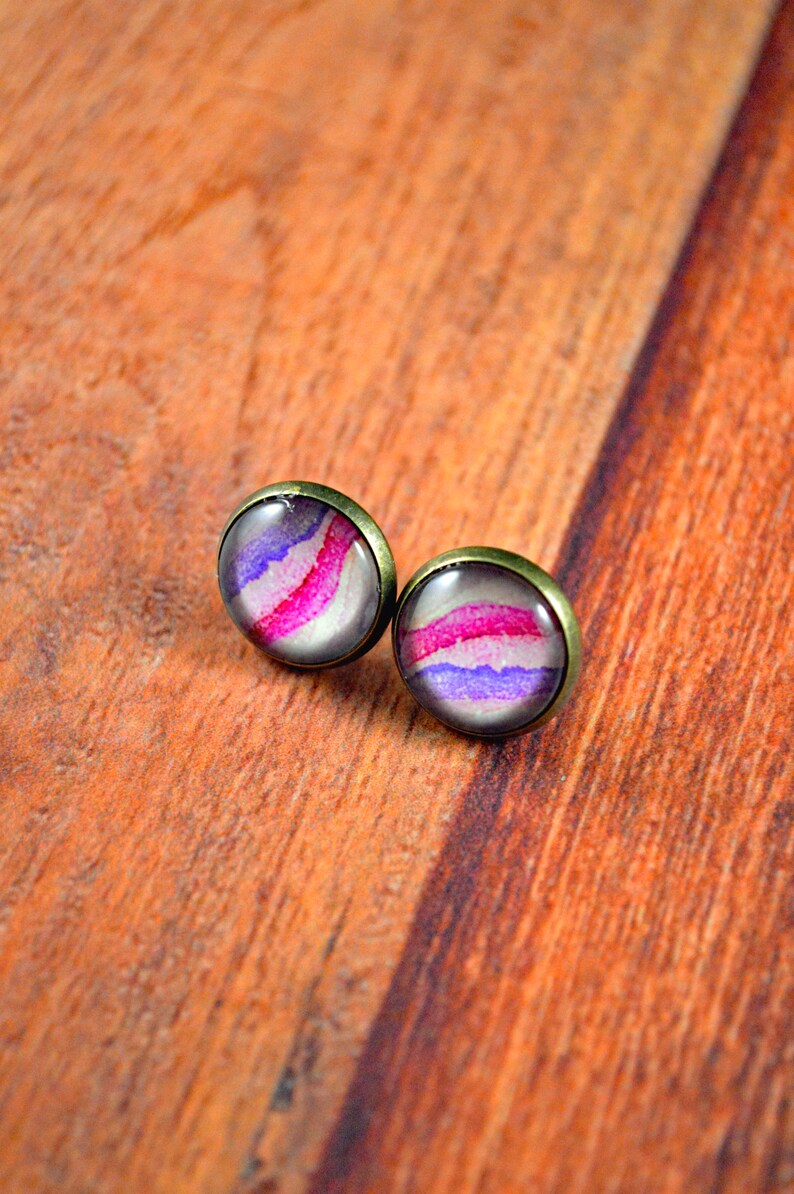 May include: A pair of stud earrings with a purple, pink, and white abstract design set in a bronze setting.