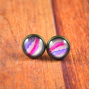 May include: A pair of stud earrings with a purple, pink, and white abstract design. The earrings have a bronze-colored metal setting.