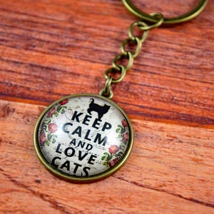 May include: A bronze key chain with a round glass charm that says "Keep Calm and Love Cats". The charm has a black silhouette of a cat and pink flowers around the edge.