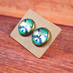 May include: A pair of round, green and white glass earrings with a raccoon design. The earrings are on a brown card.